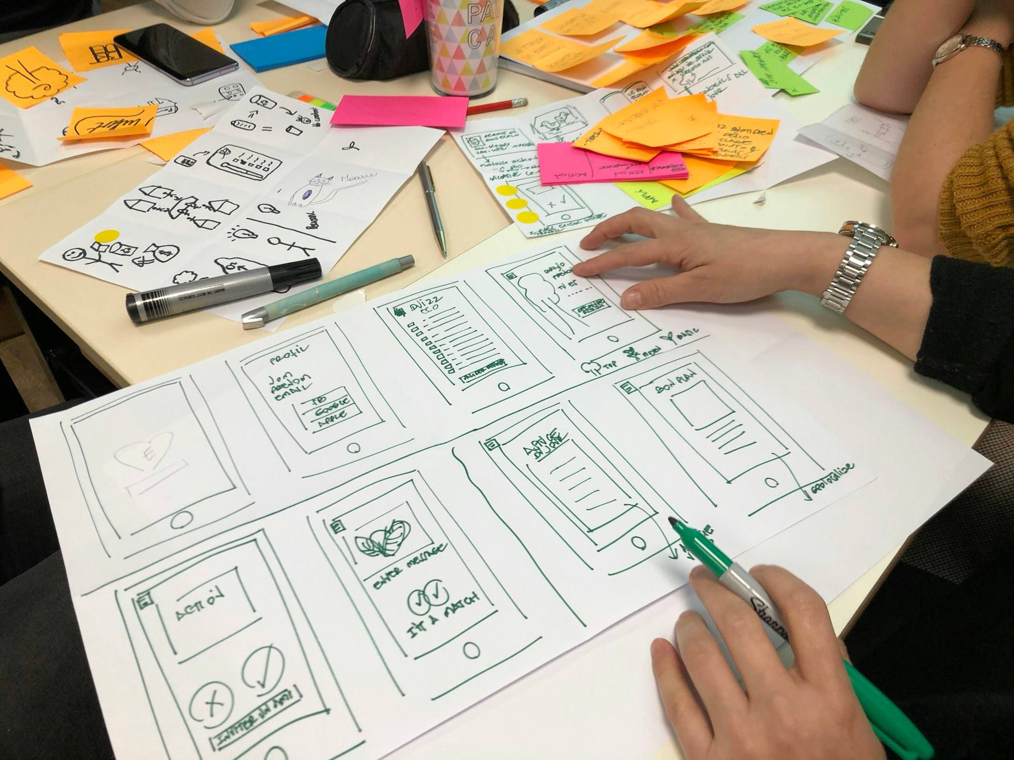Hand-drawn page layouts and sticky notes spread across a table during a planning session